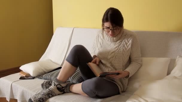 Junges Mädchen im weißen Pullover an einem Winterabend zu Hause, mit Brille, ein Buch liest und sich aufregt. Buch. Abend. Mädchen. Lesung — Stockvideo