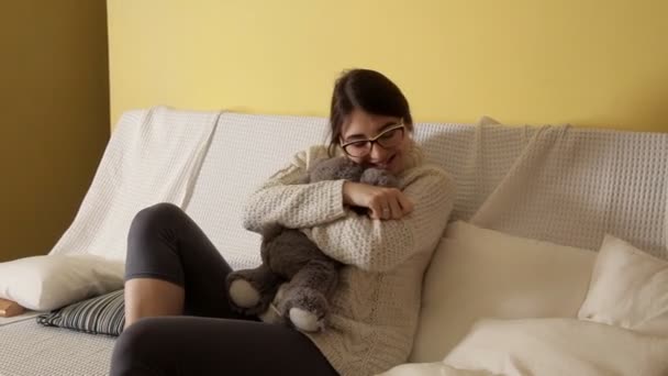 Ein junges Mädchen in weißem Pullover und Brille wird mit einem Stofftier gespielt. Kindheit. Spielzeug — Stockvideo