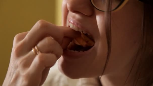 Μια νεαρή κοπέλα με τα γυαλιά, ψάχνει ενδιαφέρονται και τρώει τσιπς. Το βράδυ. Σπίτι. Άνεση. — Αρχείο Βίντεο