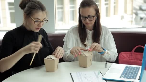 Dos chicas están sentadas en un café, comiendo fideos y discutiendo ideas de negocios. — Vídeos de Stock