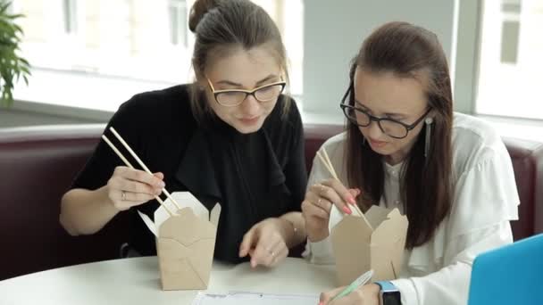 Две молодые девушки сидят в кафе, едят китайскую лапшу и планируют развитие бизнеса — стоковое видео