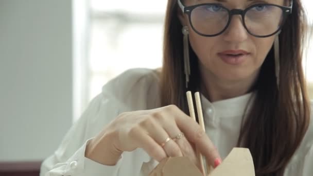 Chica de negocios con gafas come fideos en el almuerzo en el trabajo y se comunica con sus colegas. Trabajo, comida, almuerzo — Vídeo de stock