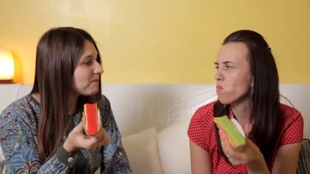 Meninas bonitas sentam-se no sofá e comem deliciosos bolos com laranja e pistache, kiwi.Friendship, comunicação, comida — Vídeo de Stock