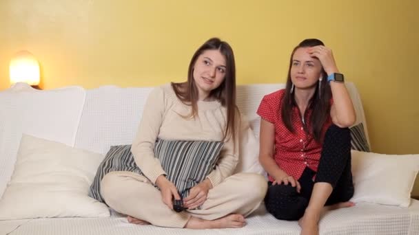 Dvě mladé dívky sedí doma na gauči, na deštivý den sledování komedie a nehýbej se. Večer domů, pohodlí, zábava — Stock video