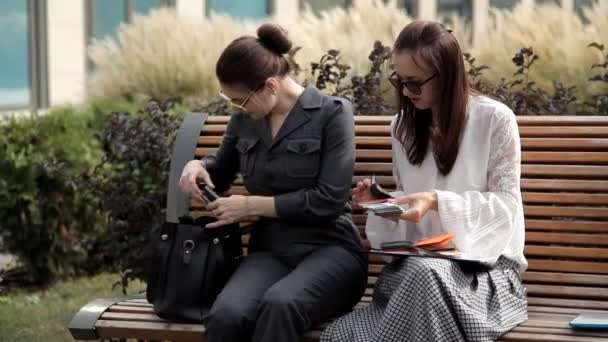 Two young business girls in the summer sitting in the Park near the business center and consider the color cards.Cutaways — Stock Video