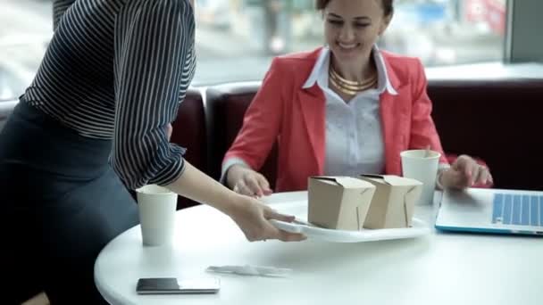 Two young business girls at lunch sitting at a laptop and eat noodles.Work, lunch — Stock Video