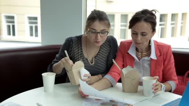 Dos jóvenes de negocios para el almuerzo comiendo fideos chinos y beber café, teniendo en cuenta el desarrollo de los negocios — Vídeos de Stock