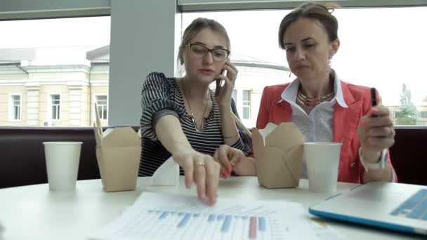 Due giovani business girl a pranzo mangiano spaghetti cinesi e bevono caffè, considerando lo sviluppo del business — Video Stock