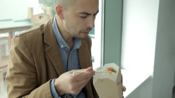 Affärsman vid panoramafönstret av affärscentret äter kinesiska nudlar. Arbete, lunch — Stockvideo