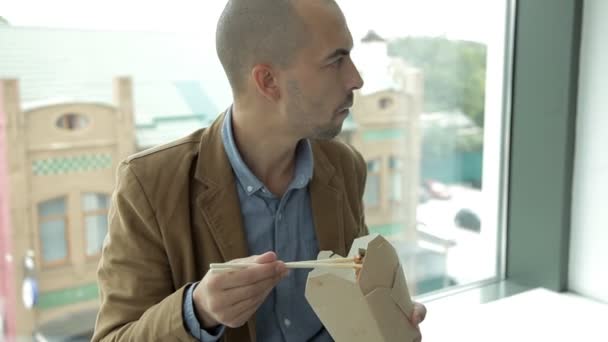 Affärsman vid panoramafönstret av affärscentret äter kinesiska nudlar. Arbete, lunch — Stockvideo
