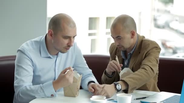Dois carecas discutem negócios ao almoço num café, a comer macarrão. Comida chinesa, centro de negócios — Vídeo de Stock