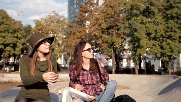 Meninas engraçadas passam tempo no parque, rir e comer um sanduíche, beber água. Dia de sanduíche, feriado — Vídeo de Stock