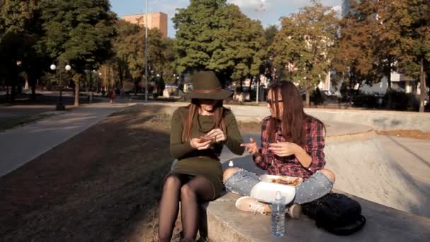 Las chicas graciosas pasan tiempo en el parque, se ríen y comen un sándwich, beben agua. Sandwich-día, día de fiesta — Vídeos de Stock