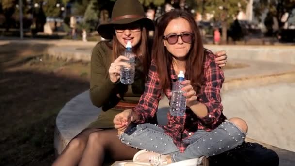 Las chicas jóvenes están sentadas en el parque, dicen, diviértanse y coman, coman un sándwich. Diversión, risa, vacaciones — Vídeos de Stock