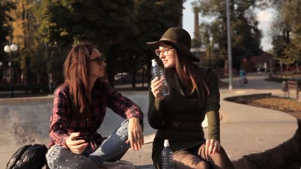 Dos chicas jóvenes están sentadas en el parque y conocen a un amigo. Alegría, reunión, descanso — Vídeo de stock