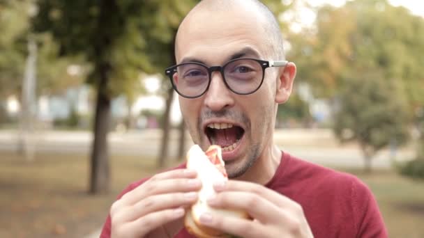 Mladá plešatý chlap v parku se snaží sendvič. Výborné jídlo, radost — Stock video