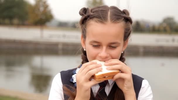 Uma criança de uniforme escolar no parque tem um delicioso sanduíche. Sandwich Holiday — Vídeo de Stock