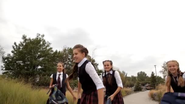 As crianças de uniforme escolar depois da escola para um passeio no parque jogam mochilas. Natureza, diversão, riso — Vídeo de Stock