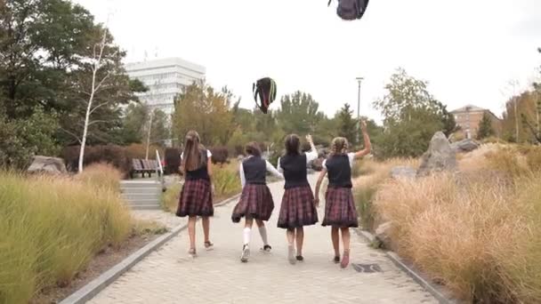 Los niños en uniforme escolar después de las clases caminan en el parque y tiran mochilas. Escuela, descanso — Vídeos de Stock