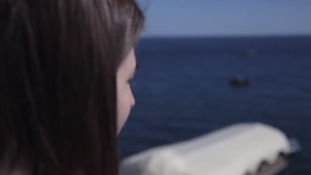 Uma jovem fica no terraço de um quarto de hotel com vista para o mar e bebe café — Vídeo de Stock