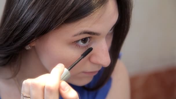 Uma jovem está de pé na frente de um espelho de maquiagem pintando os olhos com rímel — Vídeo de Stock