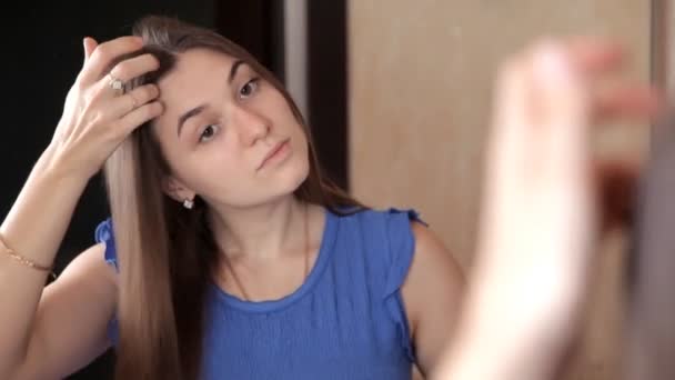 En ung flicka är stå framför en spegel och kammar sitt långa hår — Stockvideo