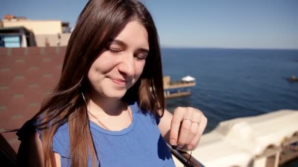 歌う音楽と踊りを聞いて海を見渡すテラスに立っている若い女の子 — ストック動画