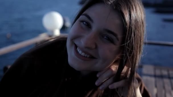 Young girl sitting by the sea smiling and posing for the camera — Stock Video