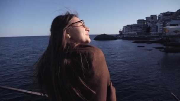 Mladá dívka stojí na molu a dívá na moře a nedaleko města můžete vidět — Stock video