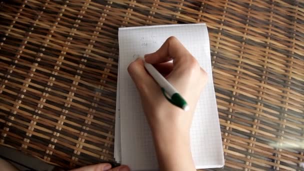Flickan sitter hemma och gör en anteckning i en anteckningsbok. Jag älskar dig — Stockvideo