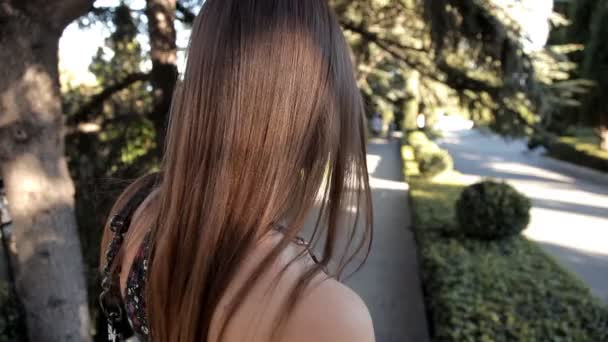 一个年轻的女孩在阳光明媚的夏天天气走在公园走在一个绿色的街道摆着相机 — 图库视频影像