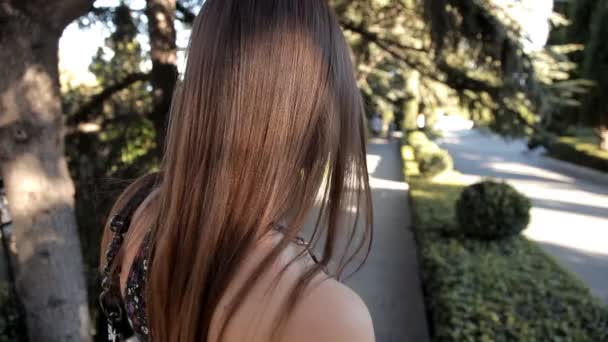 Uma jovem com clima ensolarado de verão caminha no parque andando ao longo de uma rua verde posando para a câmera — Vídeo de Stock