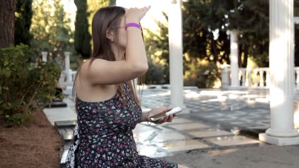 Una joven caminando en el parque decidió sentarse cerca de las hermosas columnas en anticipación de su amigo — Vídeo de stock