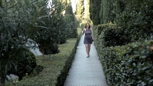 Una joven camina a lo largo de un hermoso callejón con vegetación cuando ve la diversión de la cámara corre hacia ella — Vídeo de stock