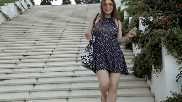Молода дівчина спускається по великих сходах з квітами на сходах, танцюючи — стокове відео