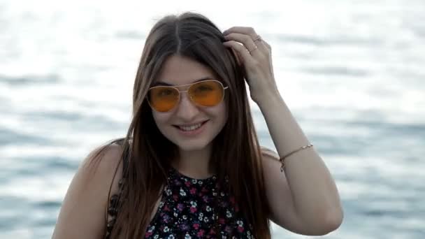 Nettes Mädchen, das bei Sonnenuntergang am Meer spaziert und vor der Kamera posiert — Stockvideo