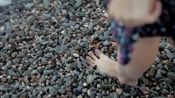 Chica caminando en la playa con pequeñas piedras de colores de sus piernas en el mar — Vídeos de Stock