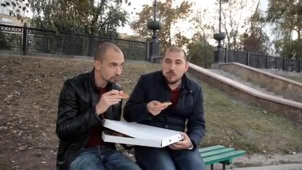 Zwei Jungs sitzen im Park und essen Pizza mit Huhn und unterhalten sich — Stockvideo