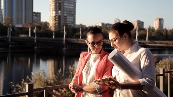 Architekci dwie dziewczyny stoją nad rzeką i omówienia projektu budowlanego. Biznes, budownictwo — Wideo stockowe