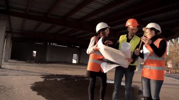 Um construtor masculino e arquitetos do sexo feminino estão revisando e discutindo um plano para a construção de um novo centro comercial. Construção, desenvolvimento, ideias — Vídeo de Stock