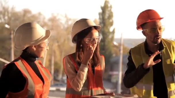 Le constructeur et les architectes féminines regardent comment la construction du nouvel objet du centre commercial est en mouvement, ils sont habillés de vêtements spéciaux et casques à des fins de sécurité — Video