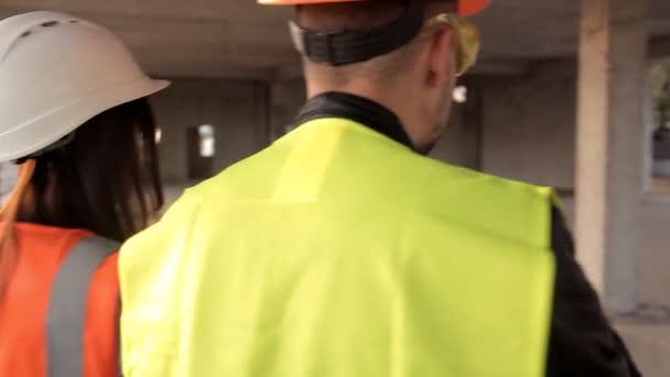 Будівельник і архітектори-жінки спостерігають, як рухається будівництво нового об'єкта торгового центру, вони одягнені в спеціальний одяг і шоломи для цілей безпеки — стокове відео