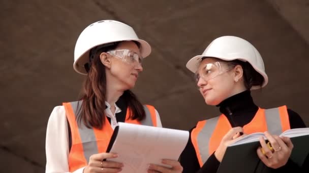 Architektinnen im Bauwesen in besonderer Form und in Helmen überprüfen und diskutieren, wie ihr Projekt entsteht — Stockvideo