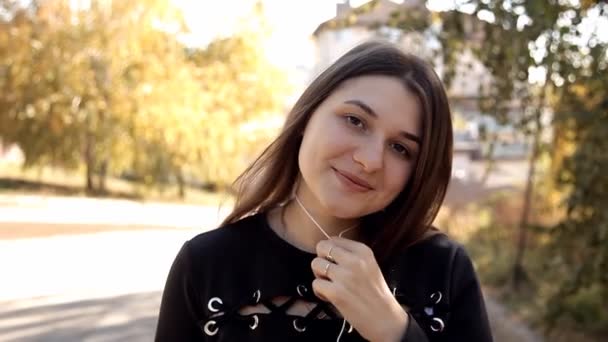 Bella ragazza che guarda la macchina fotografica e sorride. Ritratto di bella donna con auricolari senza fili. La tecnologia del futuro. Stile di vita sano — Video Stock