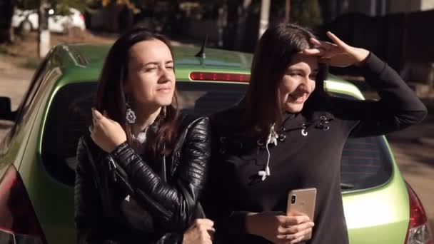 Twee vrouwen praten staan op de kap van een geparkeerde groene auto — Stockvideo