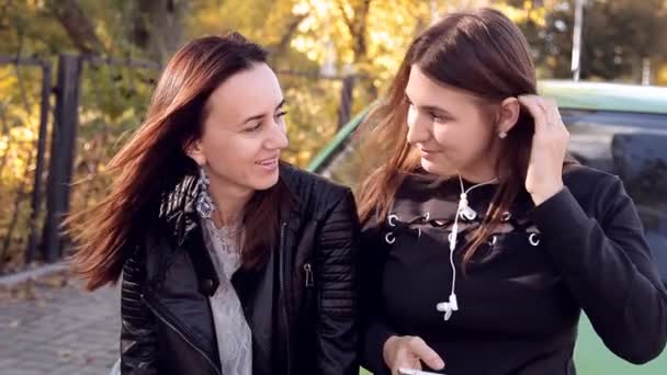 Zwei Frauen unterhalten sich stehend auf der Motorhaube eines geparkten grünen Autos — Stockvideo