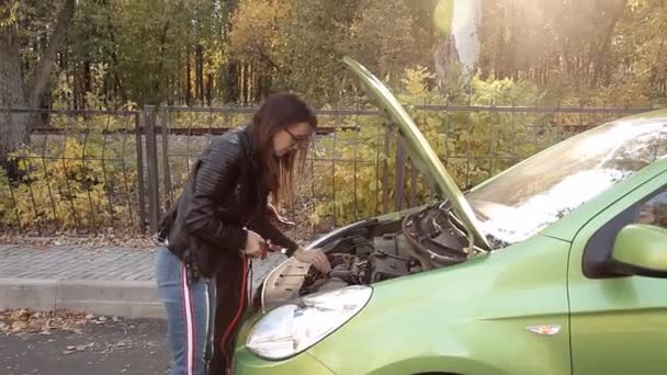 Twee niet te fel meisjes probeert een dode auto accu bij te laden. Twee meisjes op de geopende motorkap van een auto probeert te verbinden met de batterij leidt voor het opladen — Stockvideo