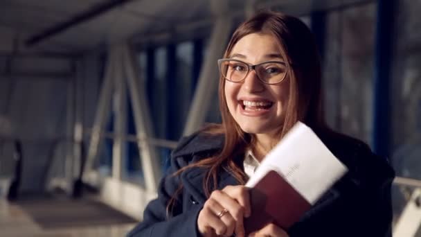 Sorrindo Jovem Mulher está segurando seu passaporte com bilhete em mãos no aeroporto. Retrato de menina bonita em óculos — Vídeo de Stock