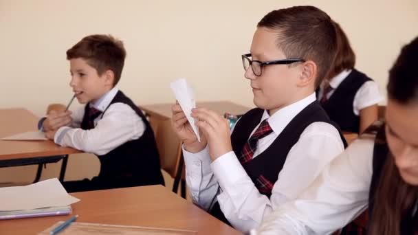 Garçon en uniforme à l'école dans la salle de classe fait l'avion de papier — Video