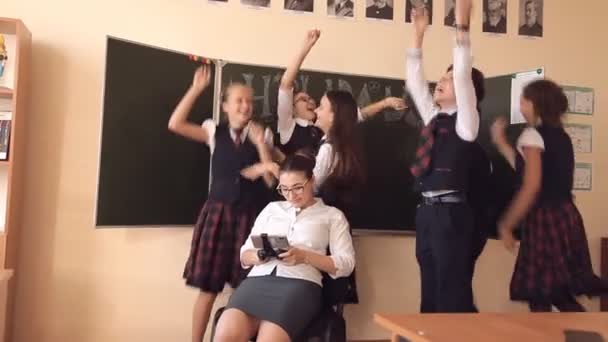 Gli alunni in uniforme scolastica sono in piedi vicino a un insegnante che è seduto su una sedia a giocare al telefono. Concetto di istruzione scolastica — Video Stock